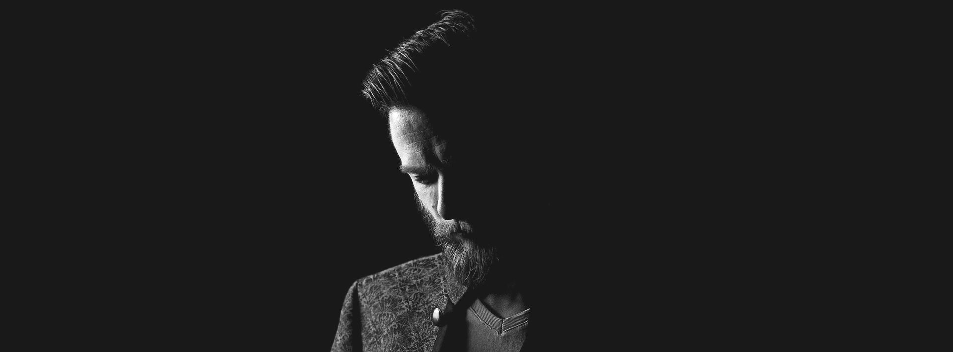 Auf einem Schwarzweißfoto blickt ein Mann mit Bart nach unten.