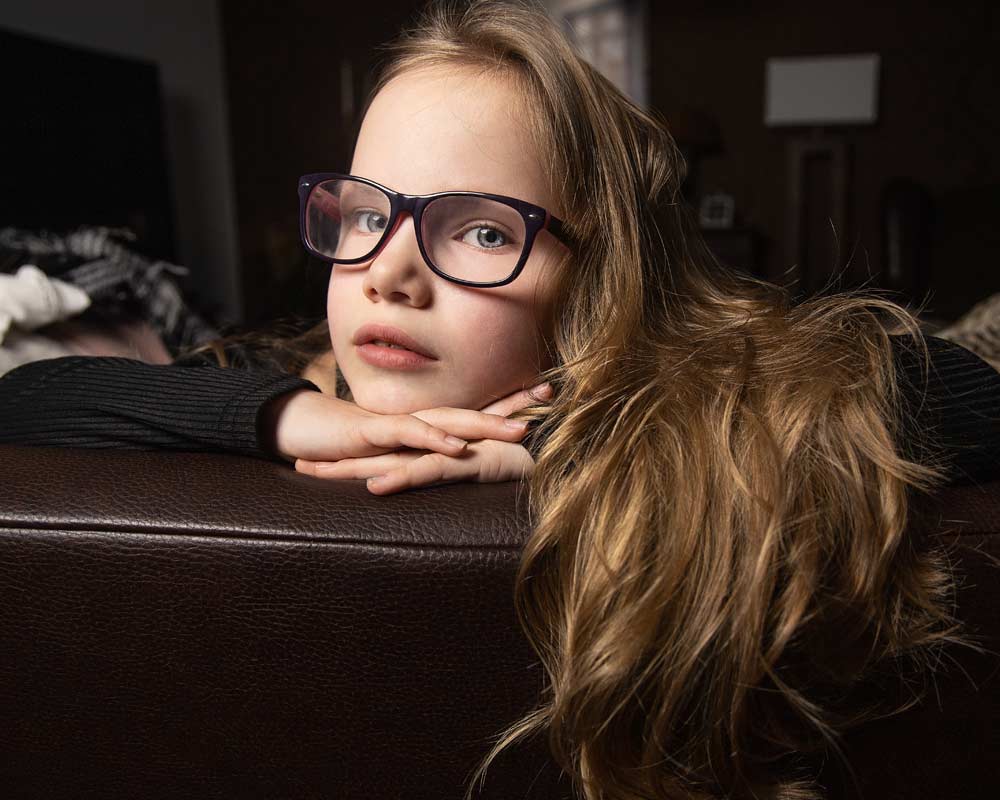 Ein kleines Mädchen mit Brille liegt auf einer Couch.