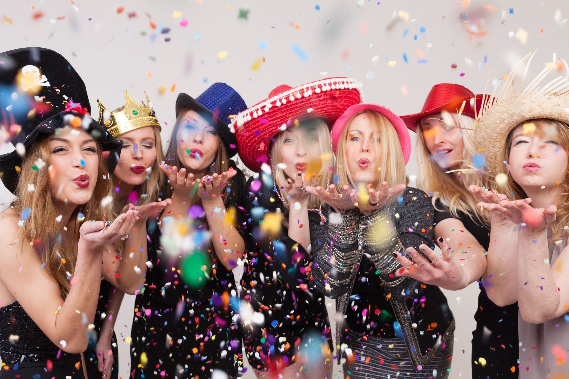 Group in party hats blowing confetti with festive expressions and colorful celebration decorations