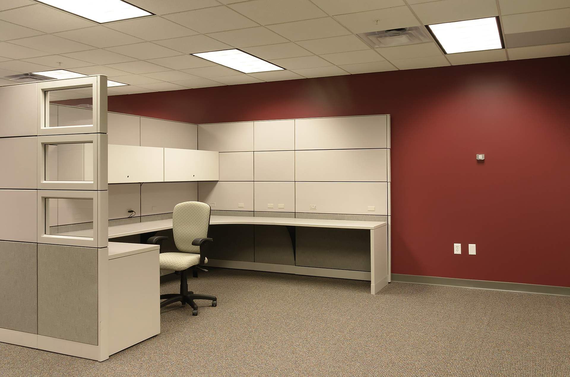 Office cubicle with desk, cabinets, chair, and red accent wall.