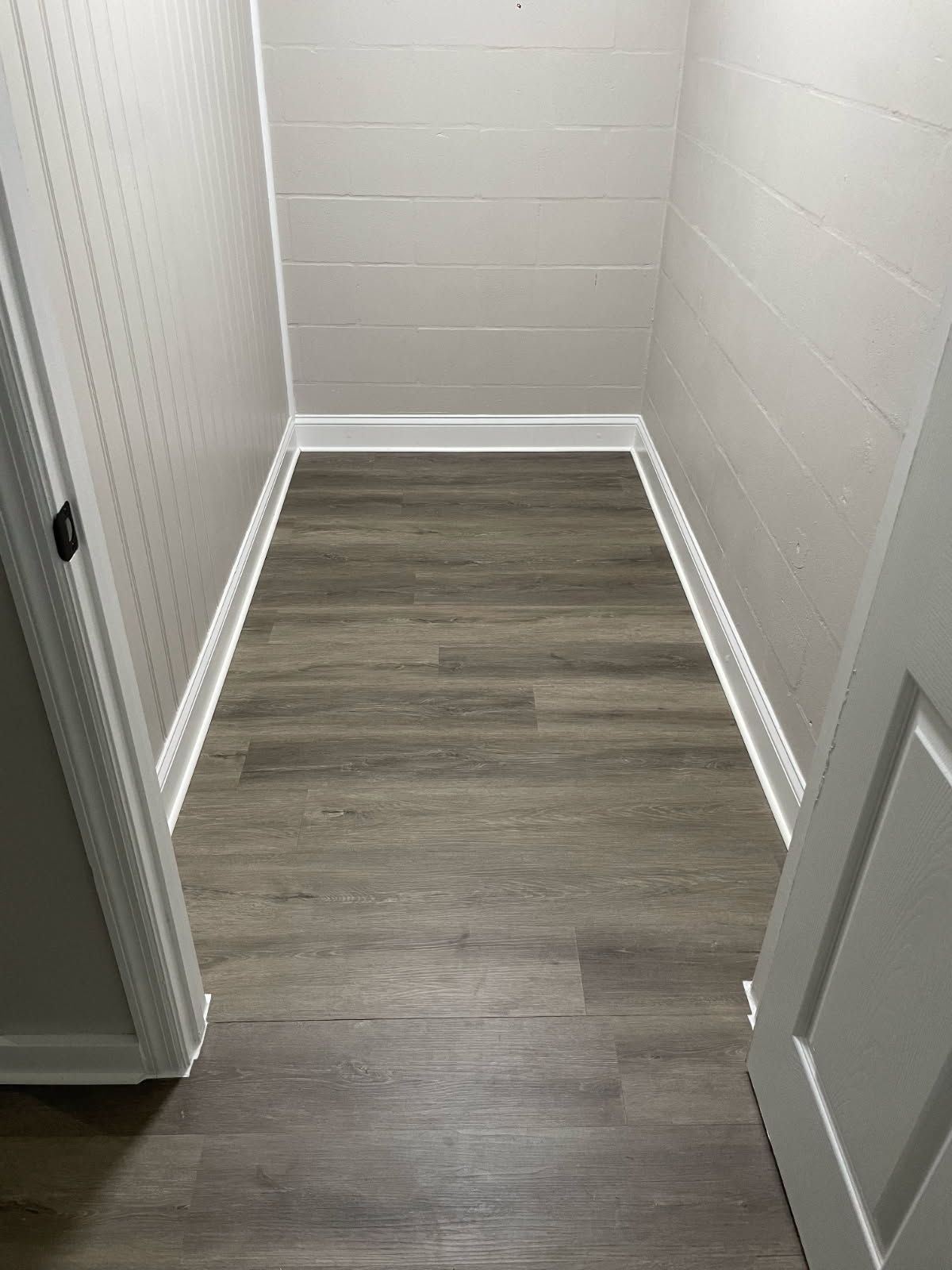 Narrow storage closet with gray wood-look floor, light gray walls, and white trim.