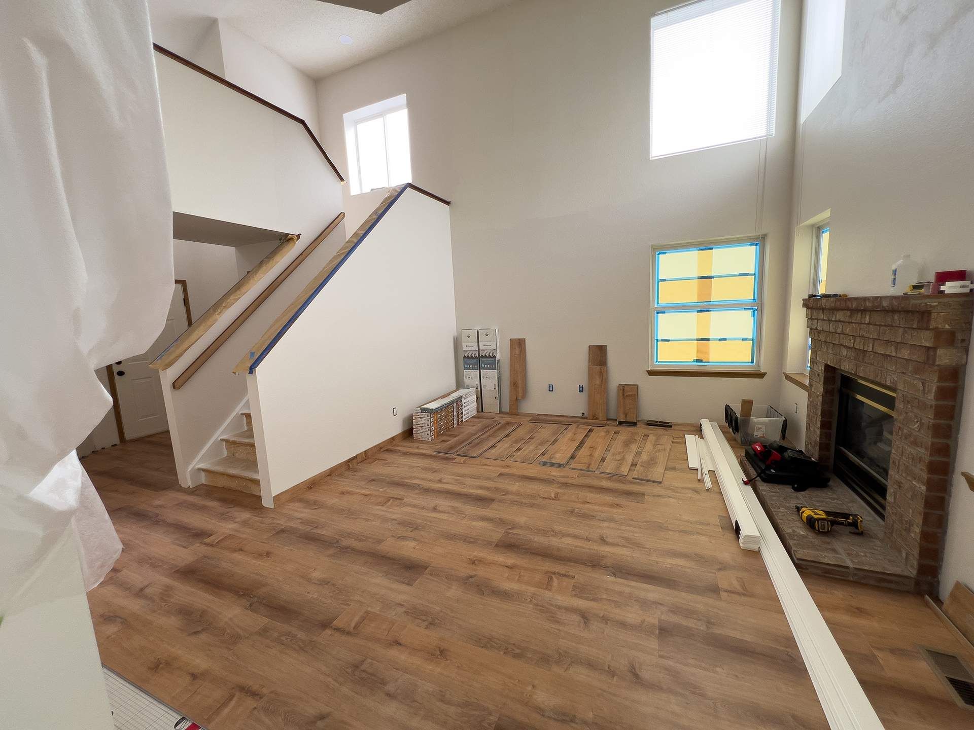 A room with new wood flooring, stairs, and a fireplace. Sunlight streams in from windows.