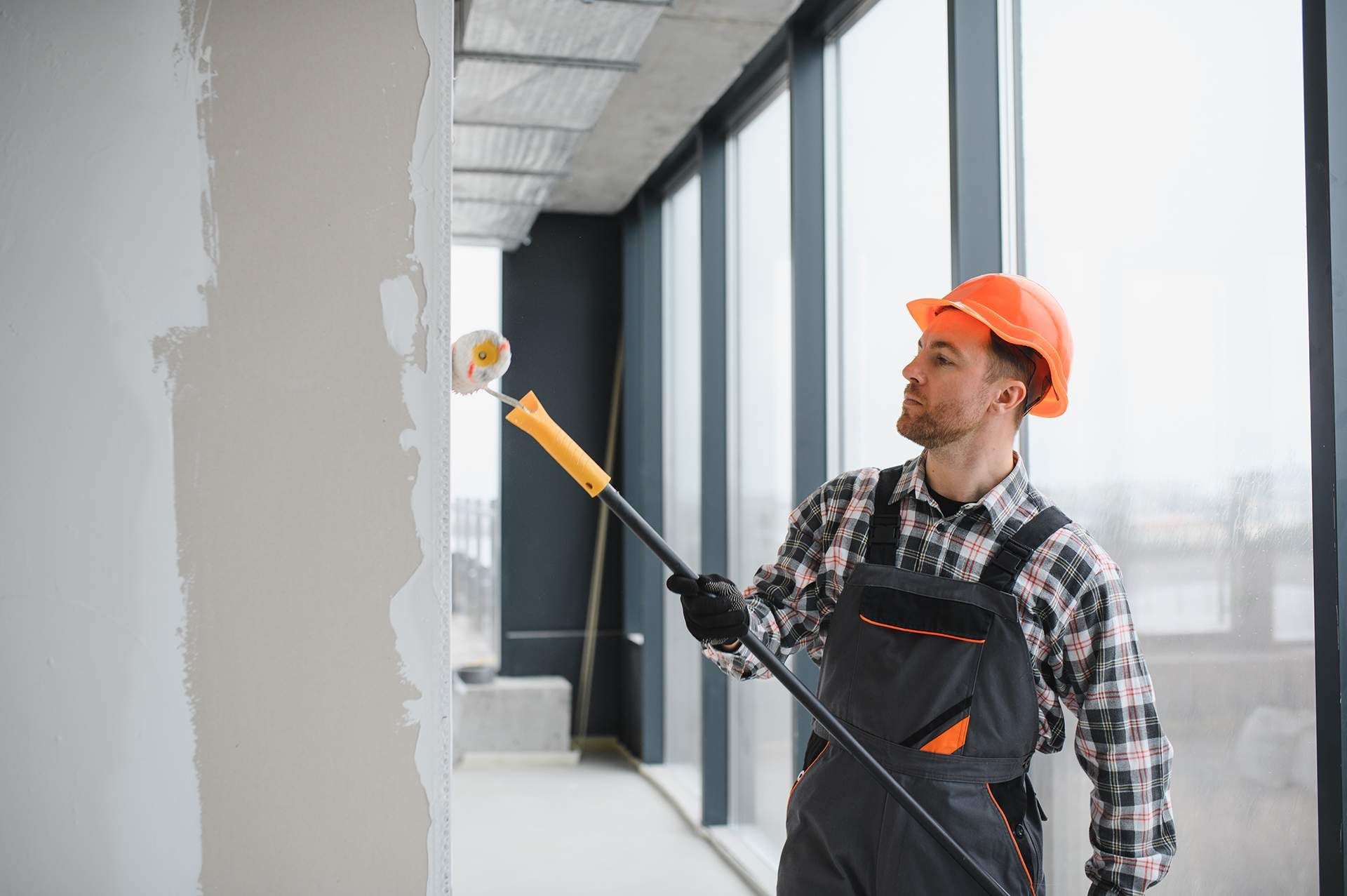 Construction worker in hard hat paints wall with roller.