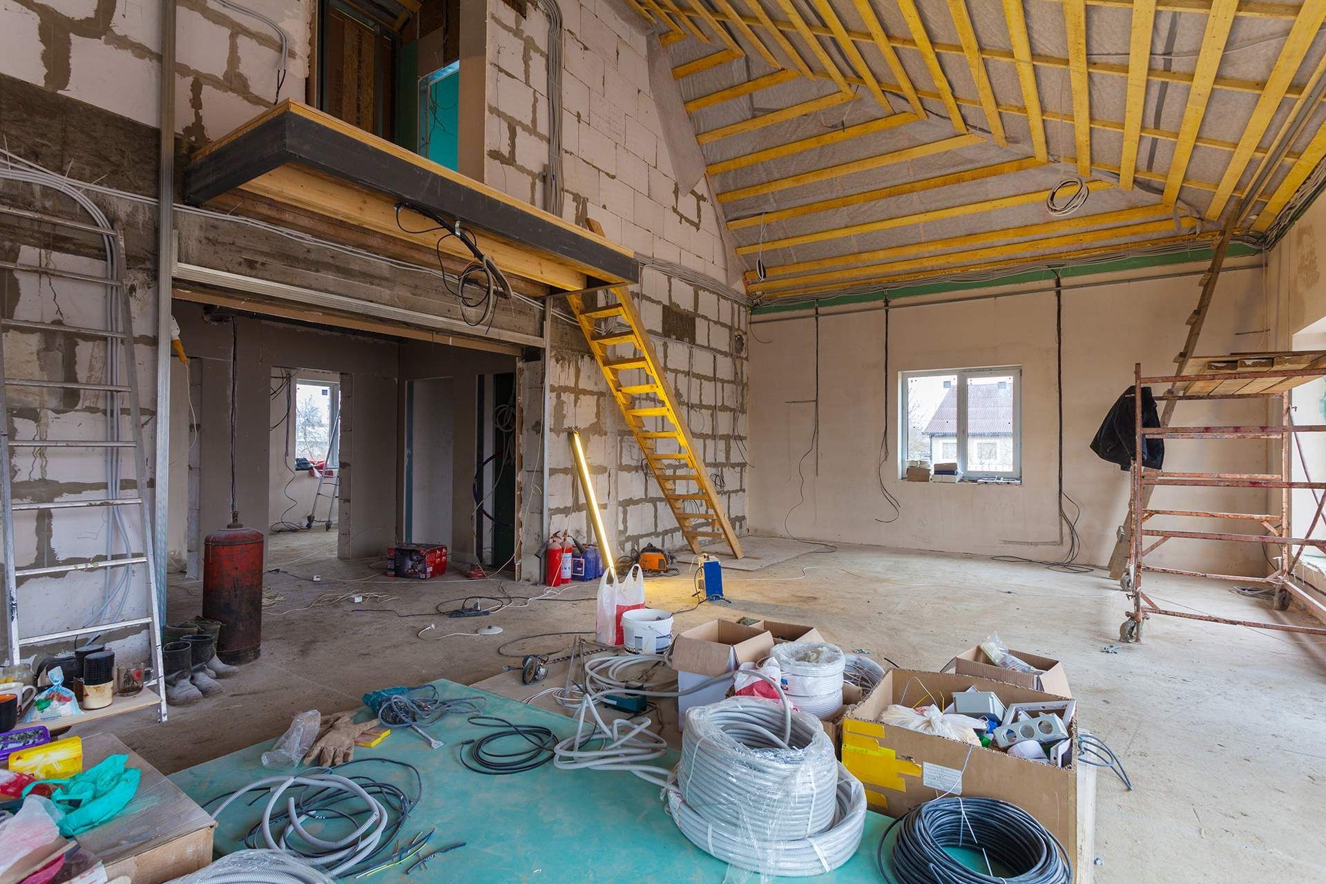 Interior of a house under construction, with exposed beams, brick walls, and construction materials scattered around.