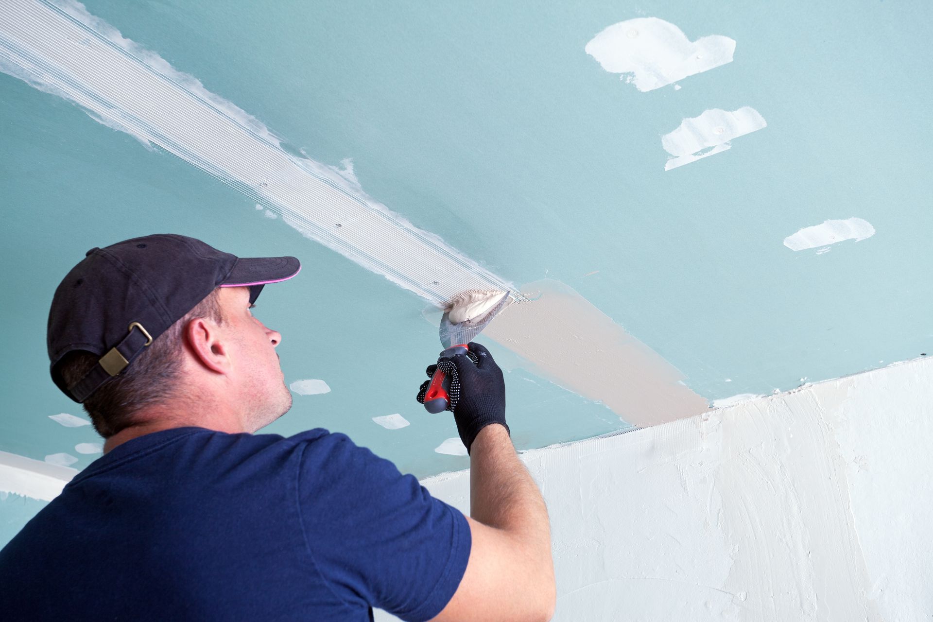 Man applying drywall compound to a ceiling with a trowel.