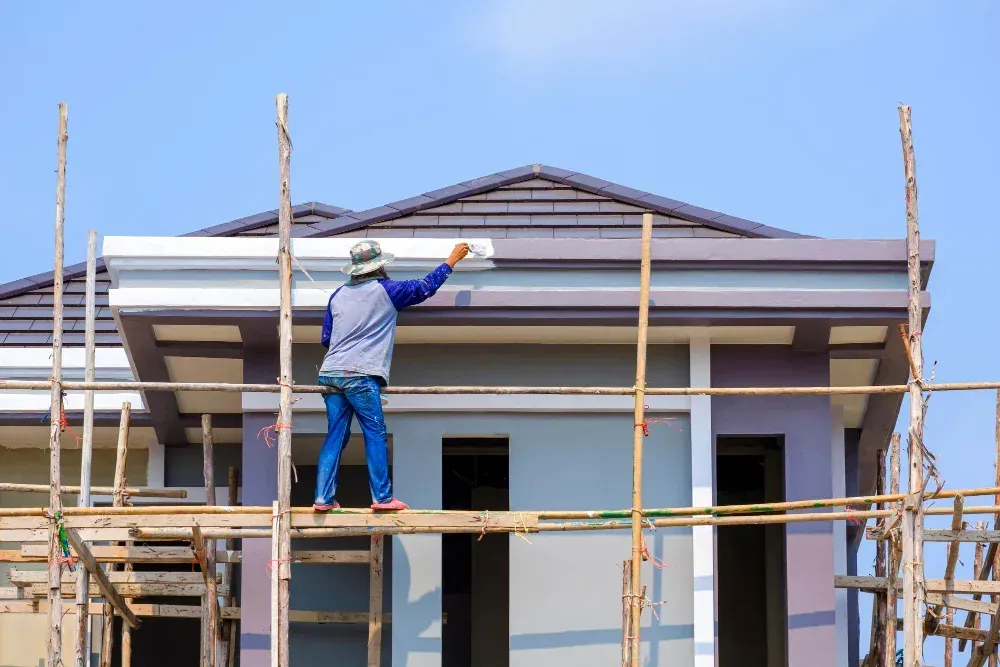 A man is standing on a scaffolding painting a house.
