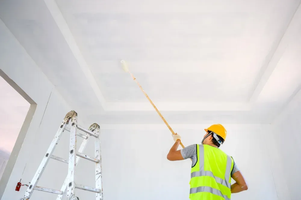 A man is painting the ceiling of a room with a paint roller.