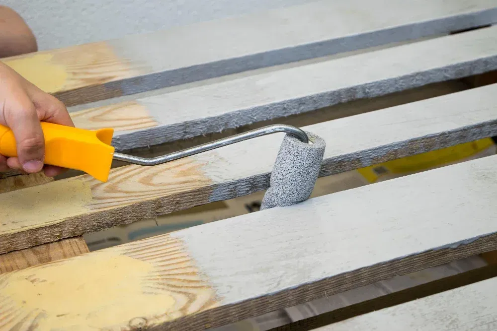 A person is painting a wooden pallet with a paint roller.