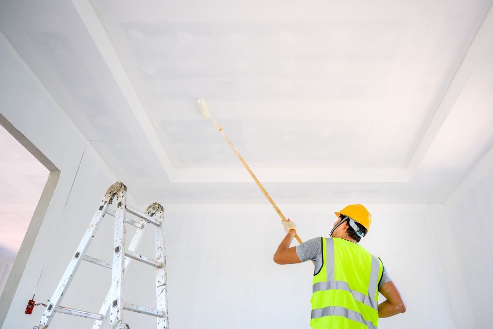 A man is painting the ceiling of a room with a paint roller.
