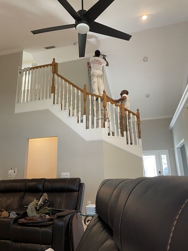 A man is painting a wall in a living room with a ceiling fan.