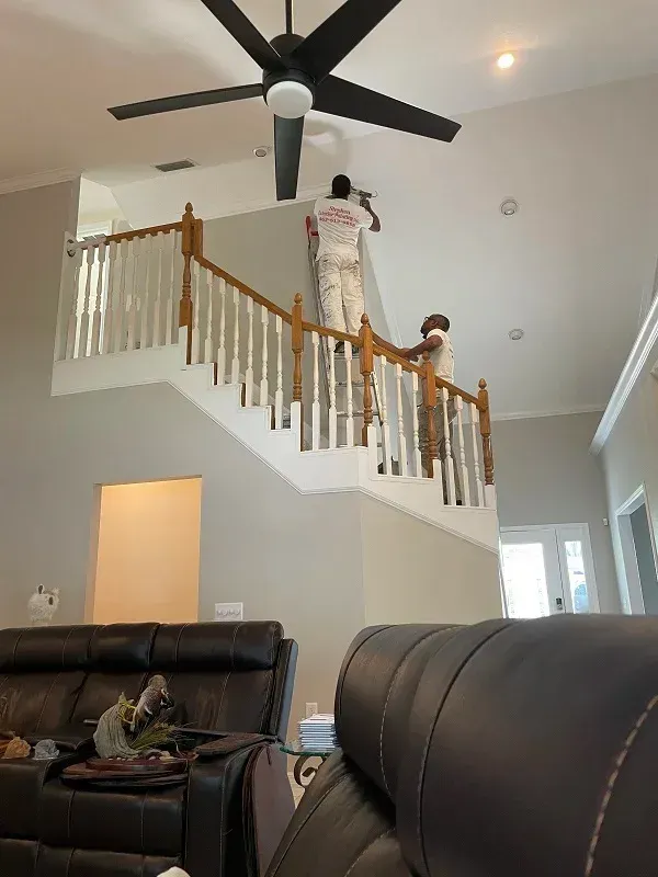 Two men are painting the stairs in a living room.