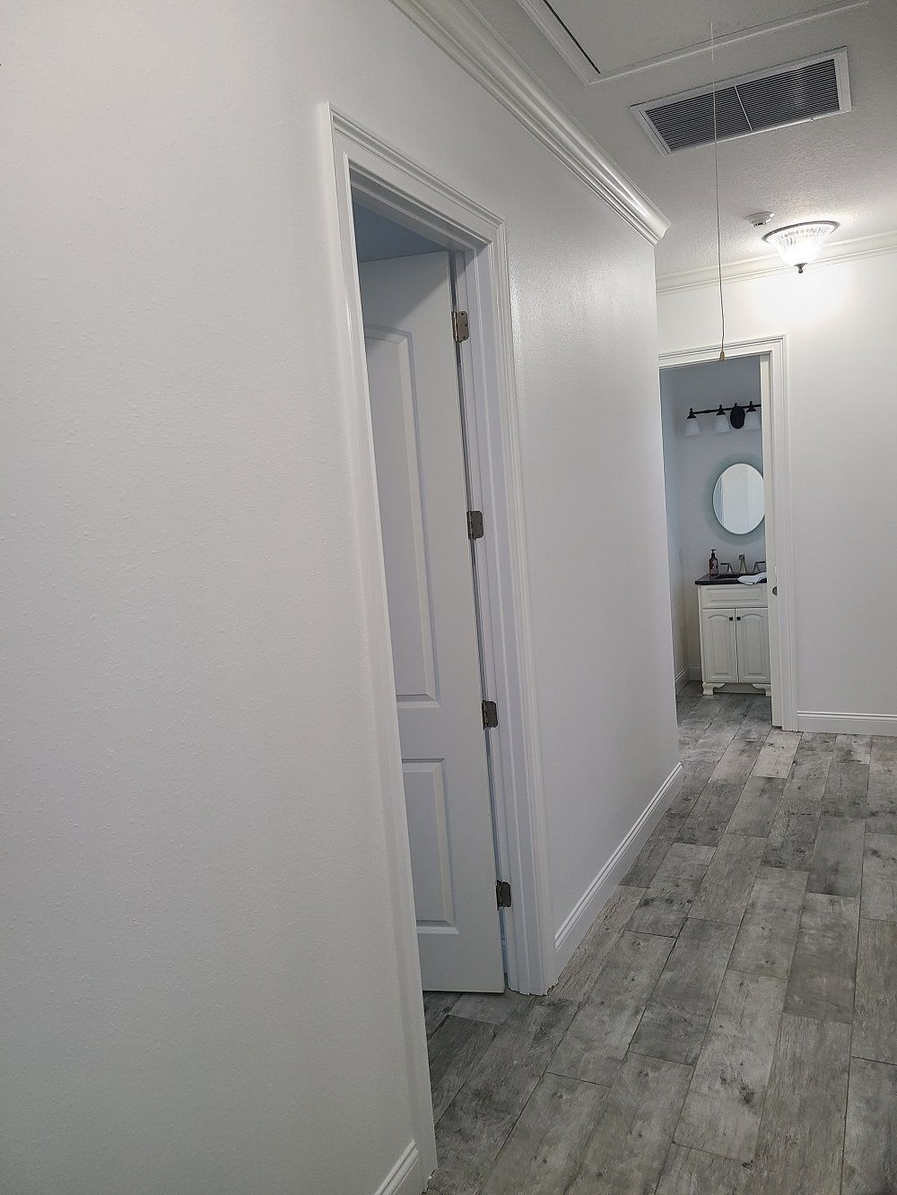 A hallway with white walls and a wooden floor leading to a bathroom.