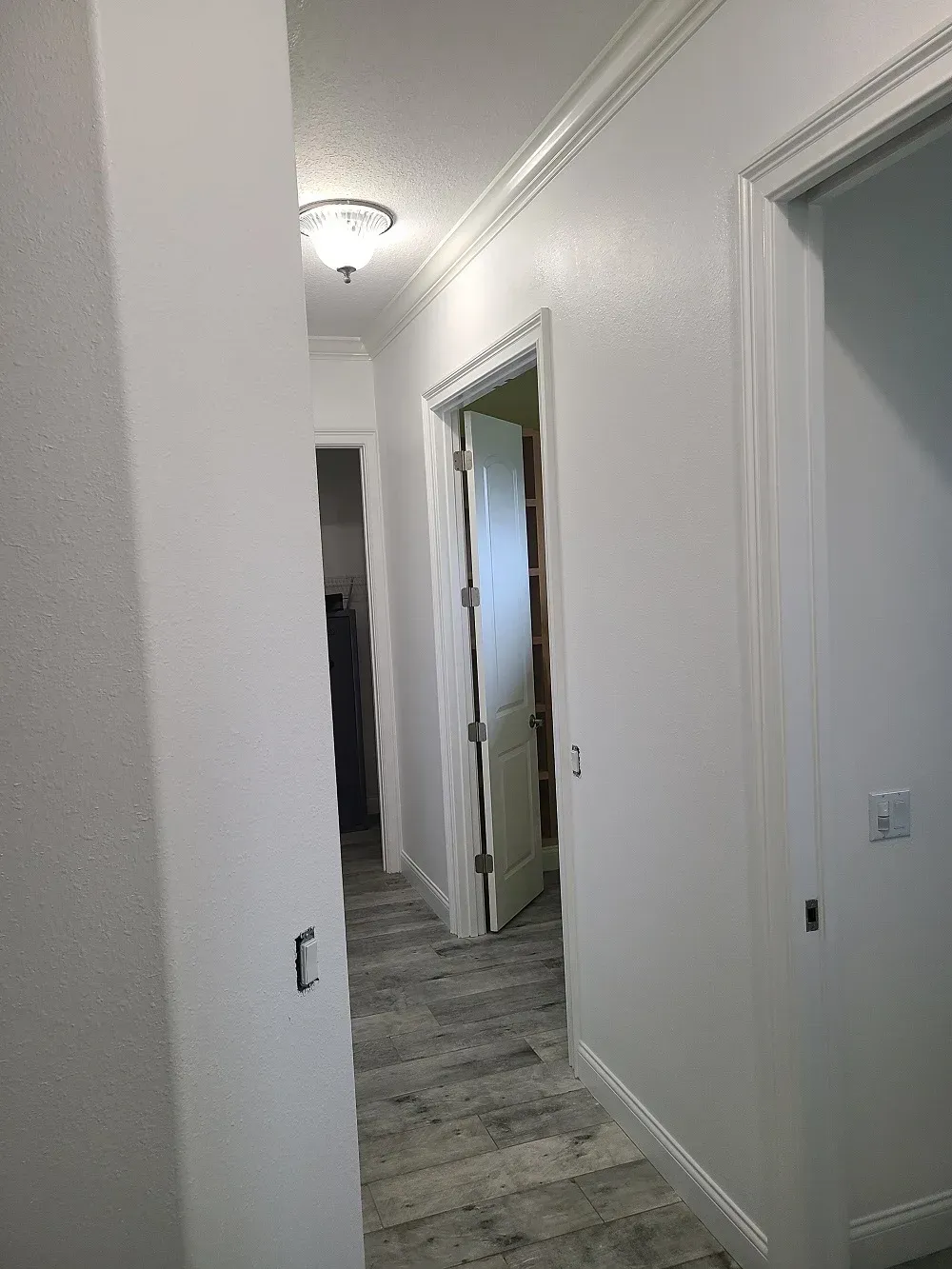 A hallway with white walls and a door leading to a bedroom.