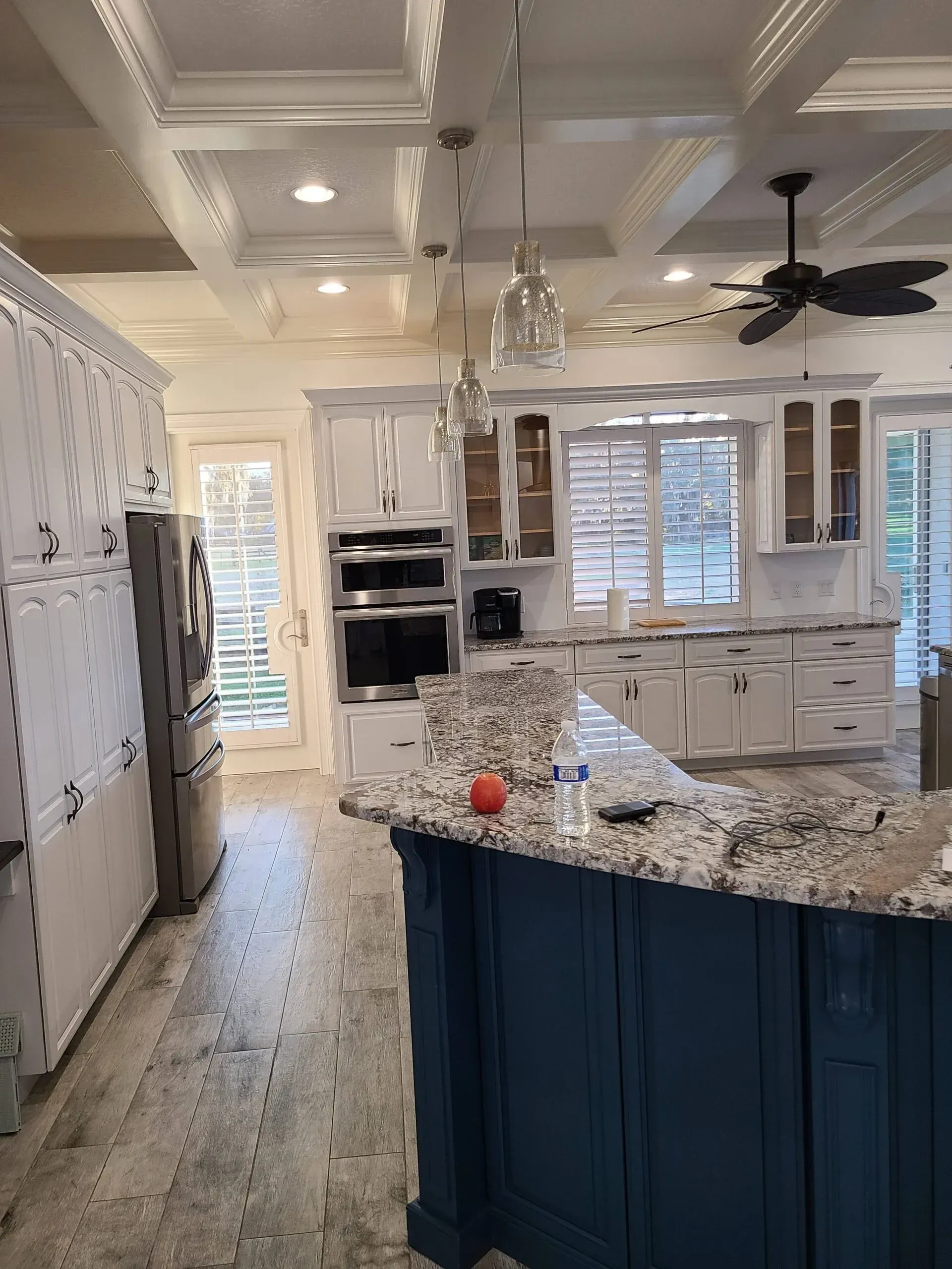 A kitchen with white cabinets , granite counter tops , and a blue island.