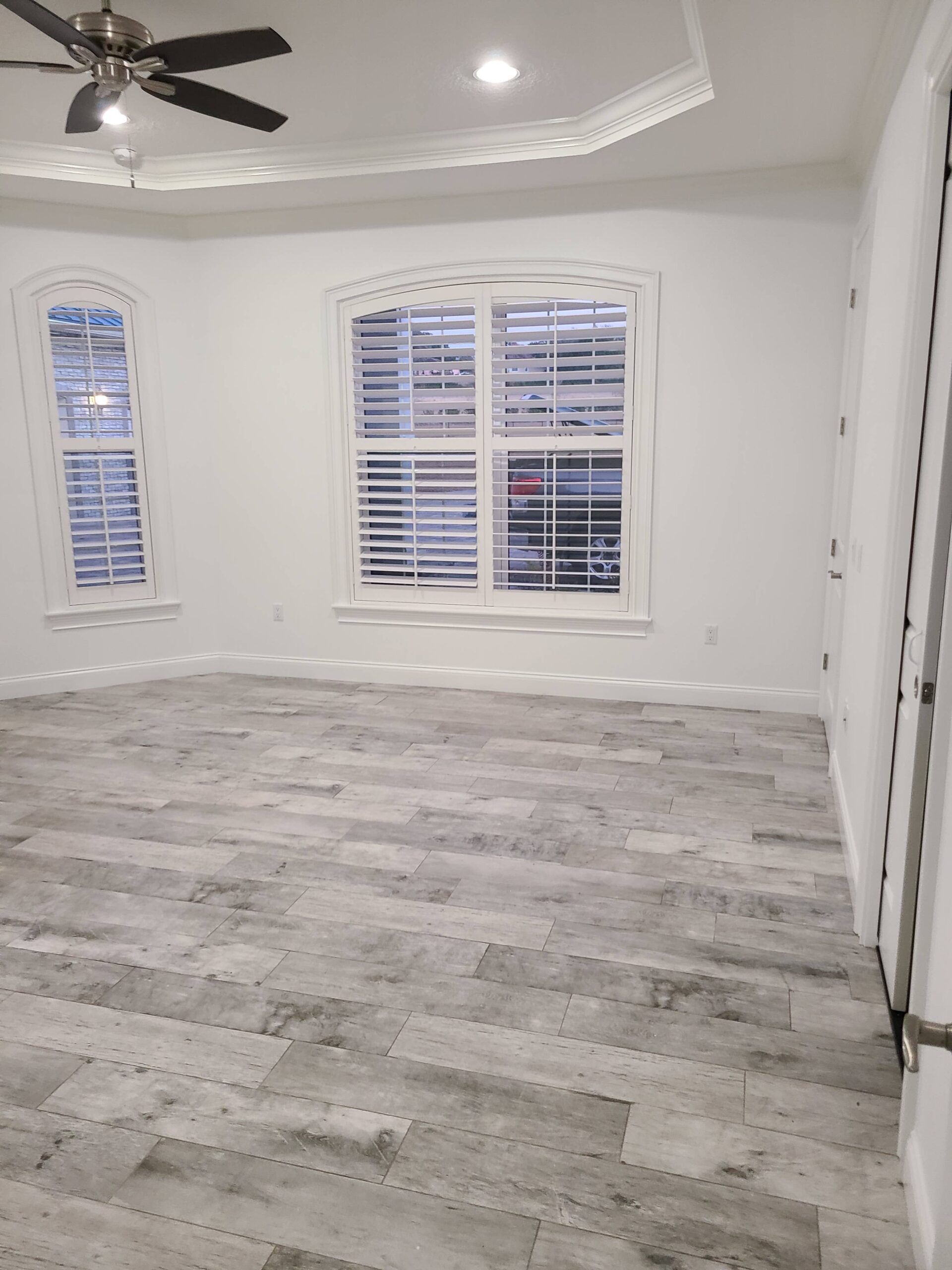 An empty room with a ceiling fan and two windows.