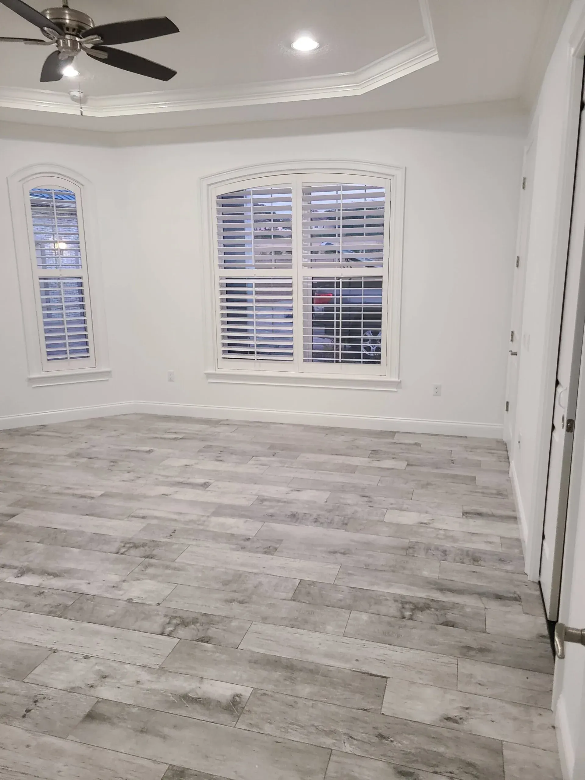 An empty room with a ceiling fan and two windows.