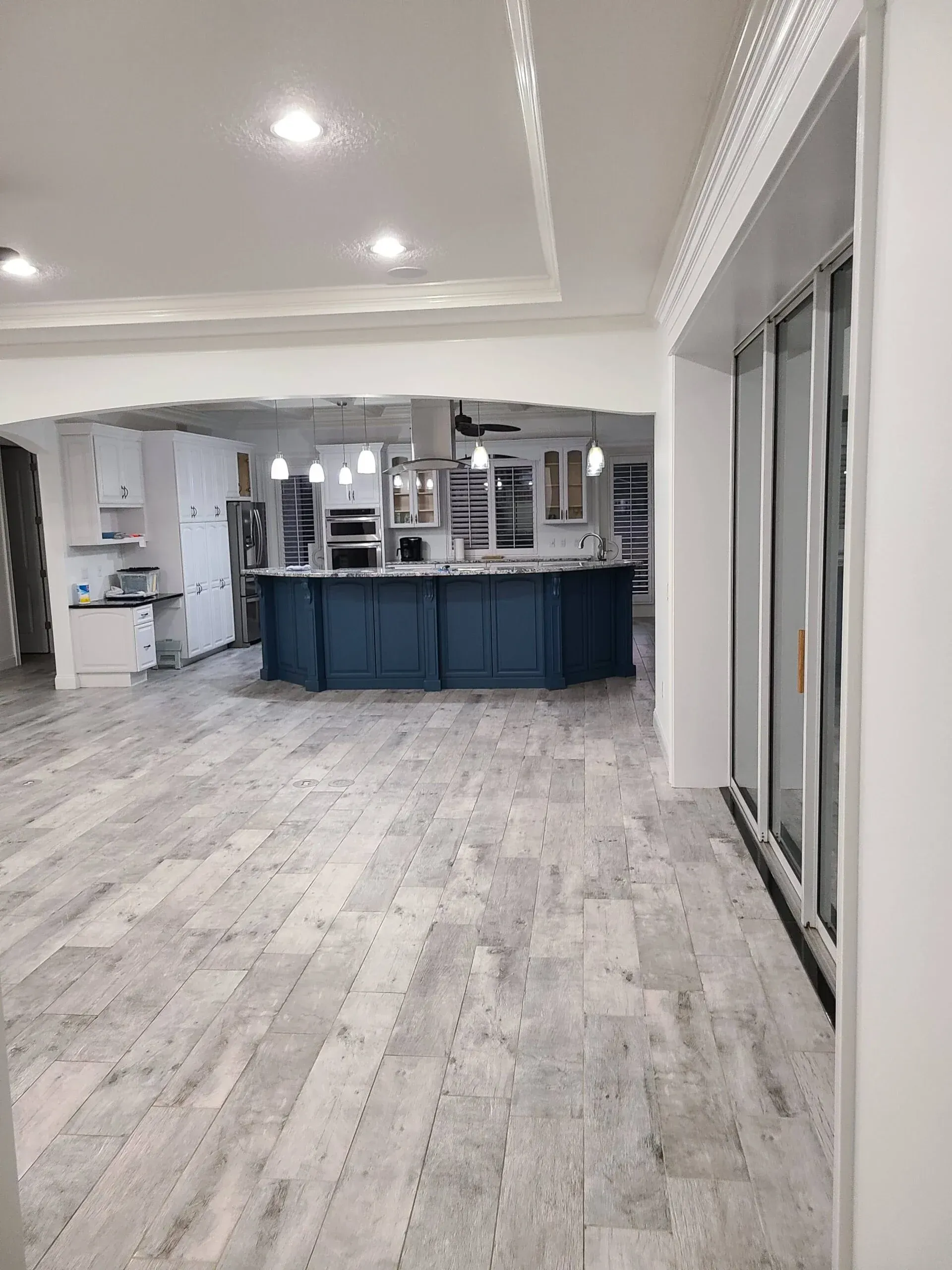 A large room with hardwood floors and a kitchen in the background.