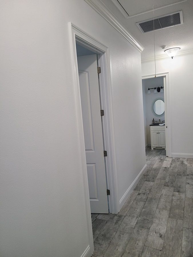A hallway with white walls and wooden floors leading to a bathroom.