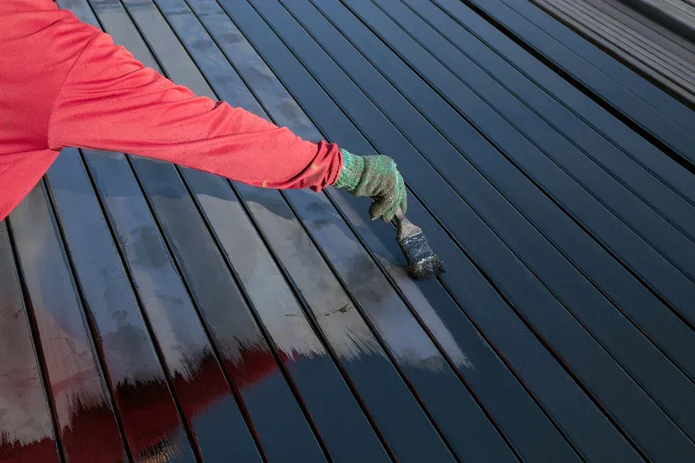 A person is painting a wooden deck with a brush.