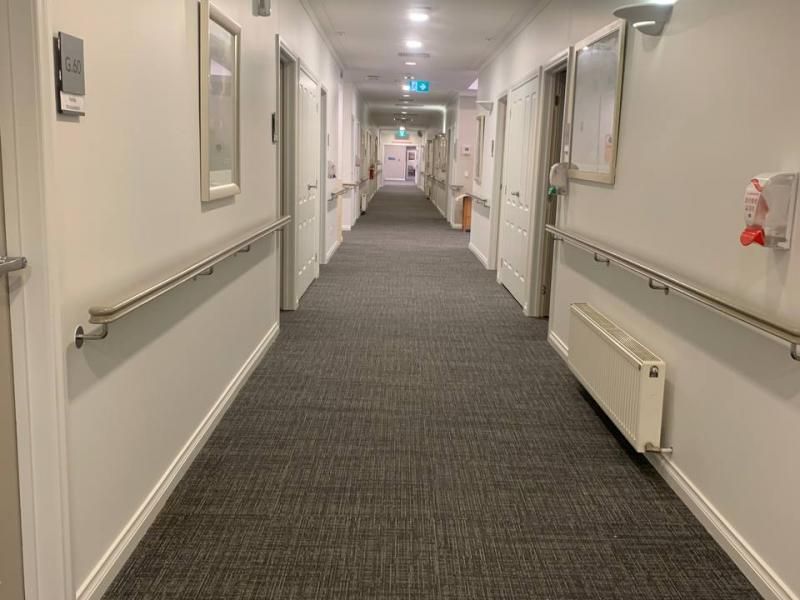 A long hallway in a hospital with a gray carpet and white walls.
