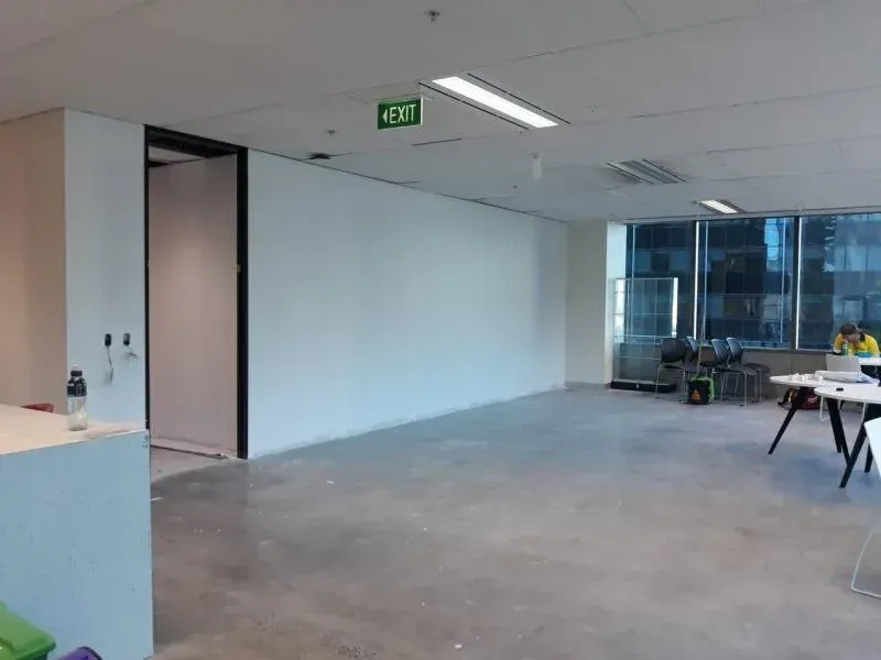 A large empty office with a green exit sign on the ceiling.