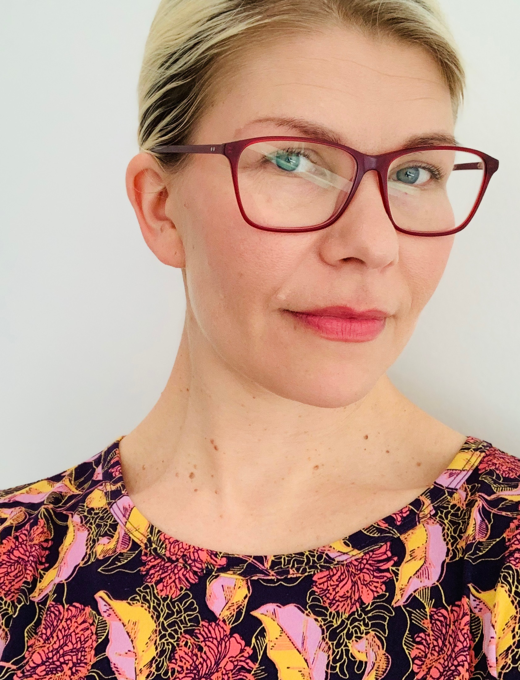 Woman wearing maroon glasses, looking at the camera.