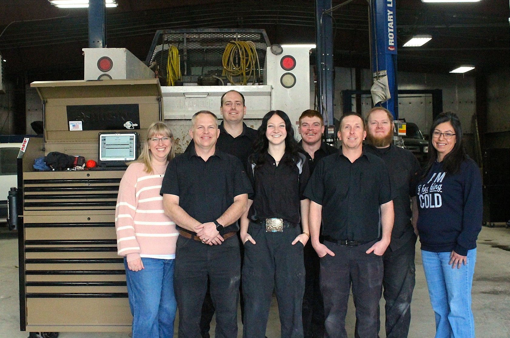 Group of seven people posing in front of a building. Six are in black shirts and pants, one in jeans | Don's Repair