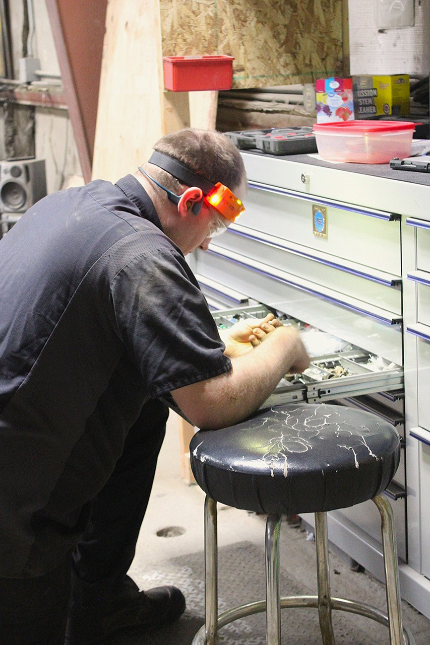 Man wearing safety glasses works at a workbench, seated on a stool | Don's Repair