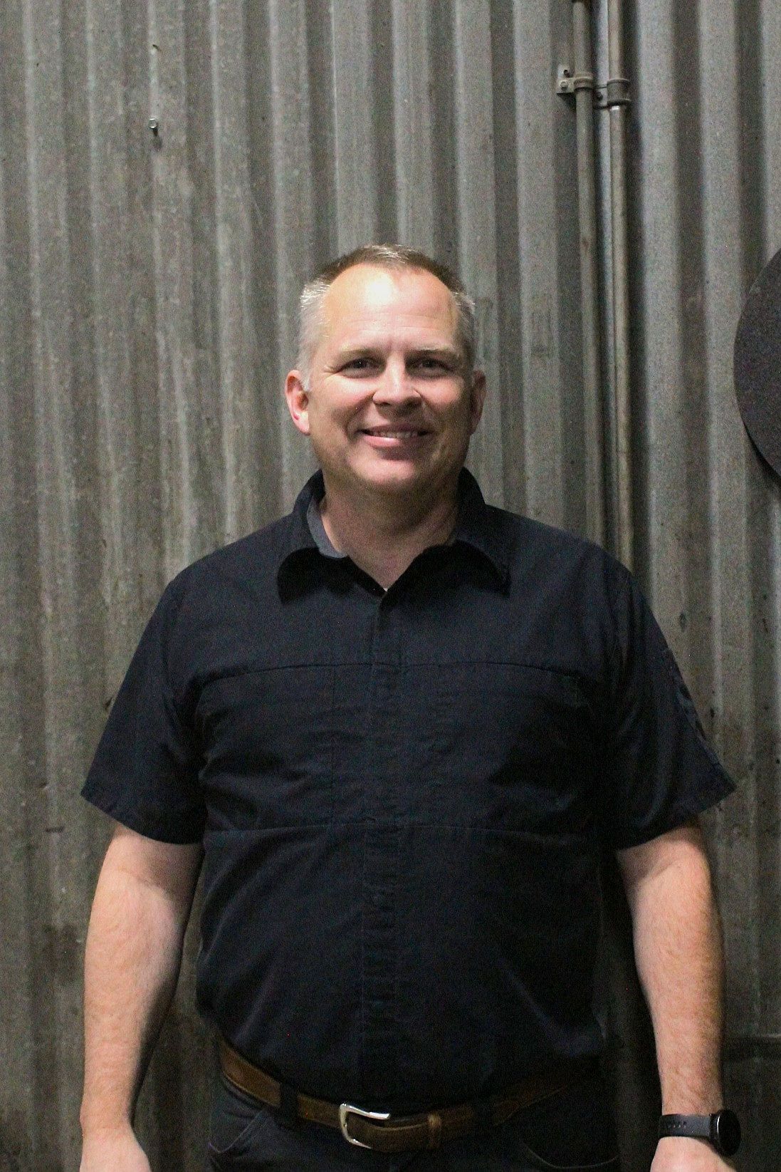 Man in black shirt smiles in front of a corrugated metal wall | Don's Repair