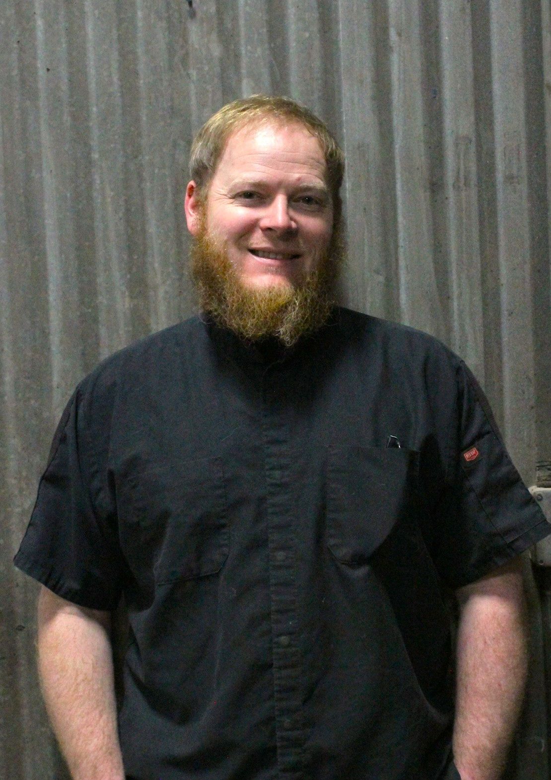 Man with a full beard, wearing a black work shirt, smiles in front of a corrugated metal wall | Don's Repair