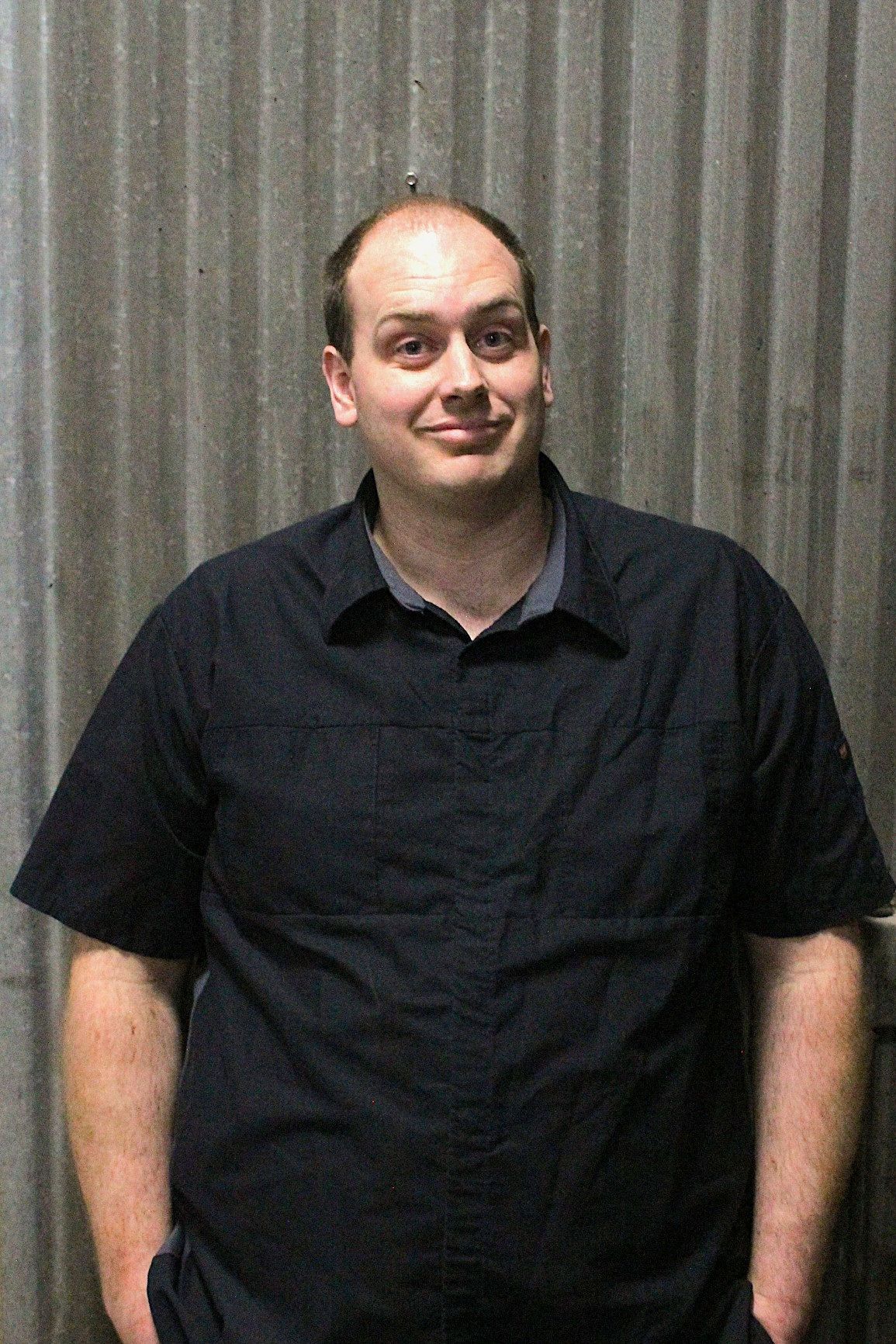 Man in dark short-sleeved shirt standing in front of corrugated metal, smiling with hands in pockets | Don's Repair