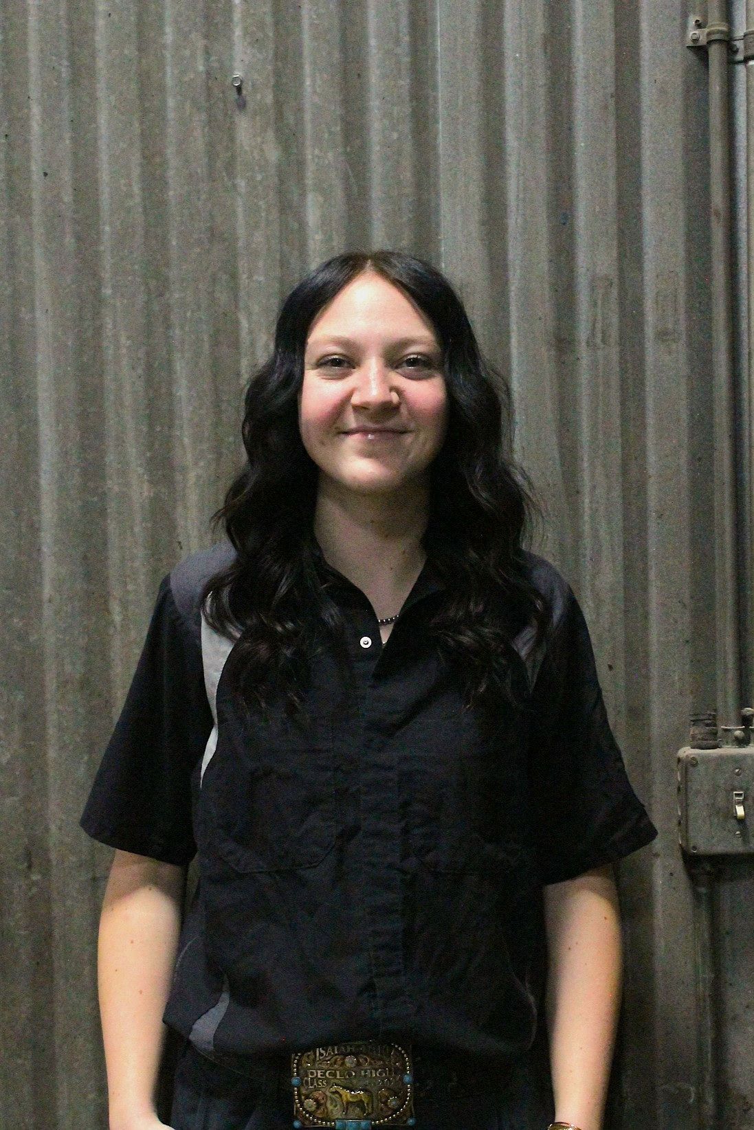Woman with dark wavy hair wearing a black shirt, smiling, standing in front of a metal wall | Don's Repair