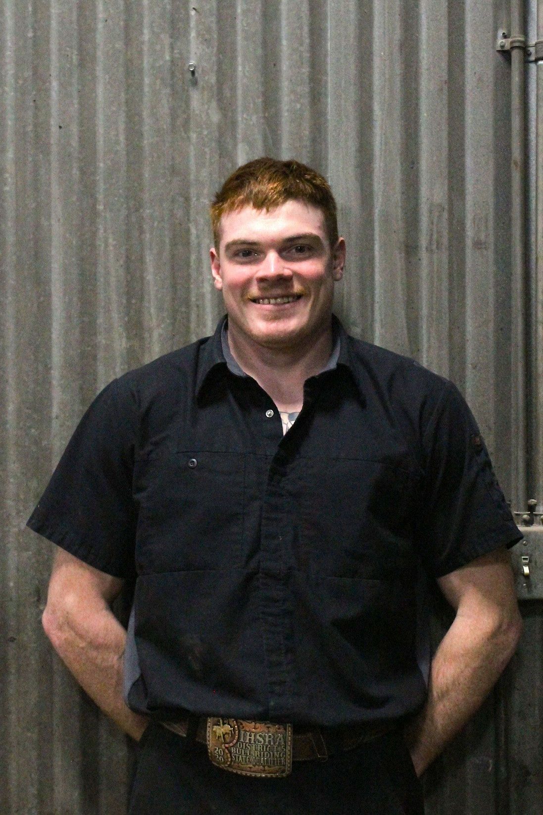 Man with red hair, smiling in a dark blue shirt and belt buckle, standing against a corrugated metal wall | Don's Repair