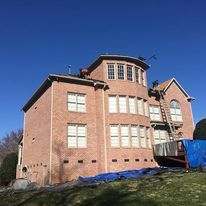 A large brick building with a roof that is being painted.
