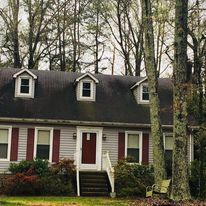 A house with a black roof and red shutters is surrounded by trees.