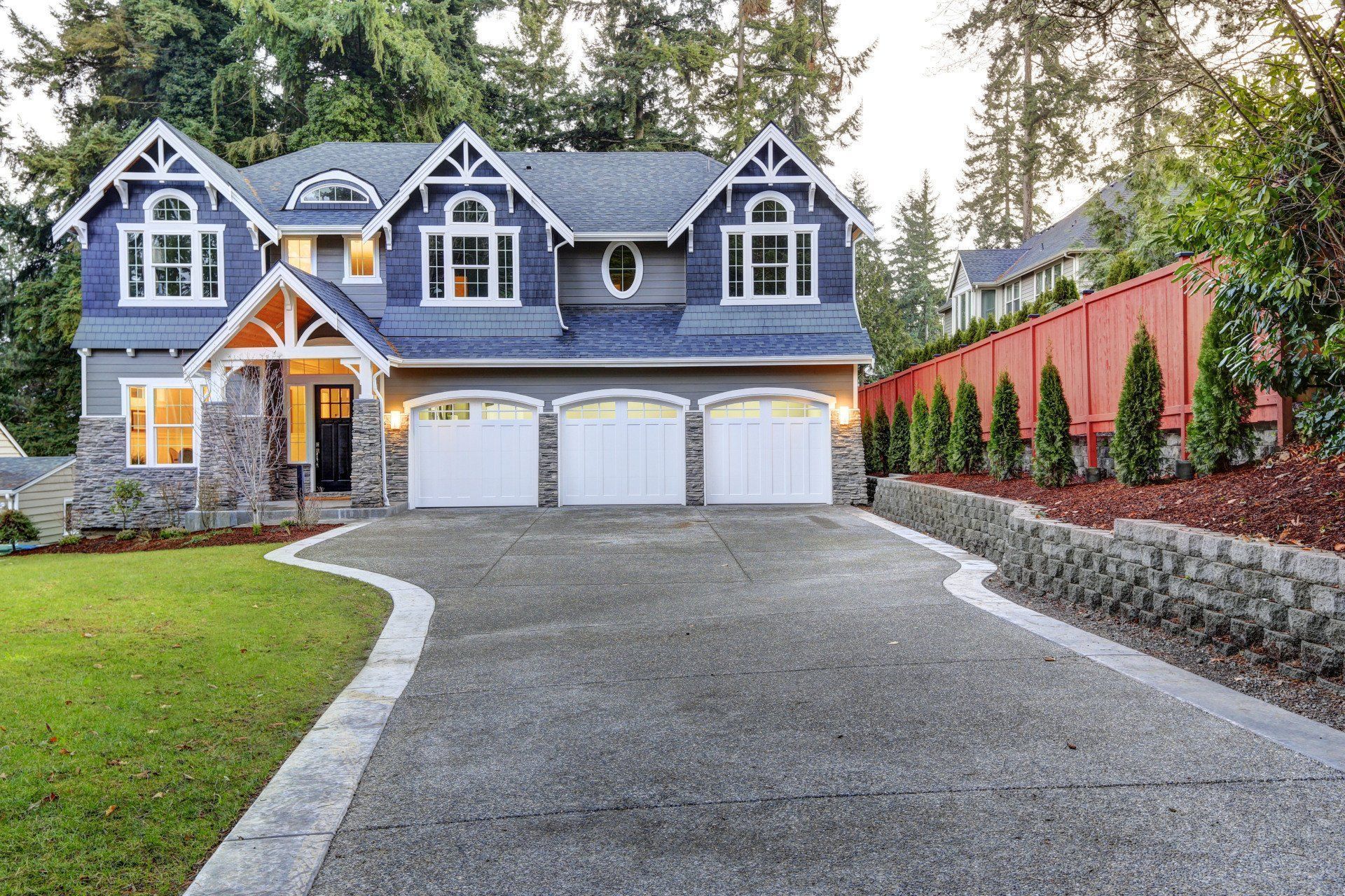 A large blue house with three garage doors and a large driveway.