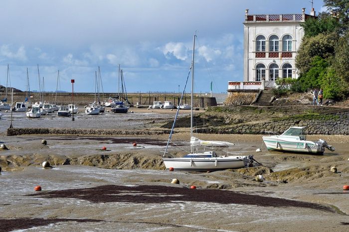 A boat is sitting on the shore of a body of water with a building in the background.