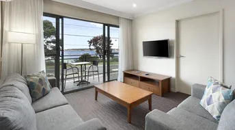 Living room with gray couches, TV, and balcony overlooking water.