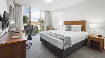 Hotel room with king bed, desk, and floor-to-ceiling window overlooking balcony.