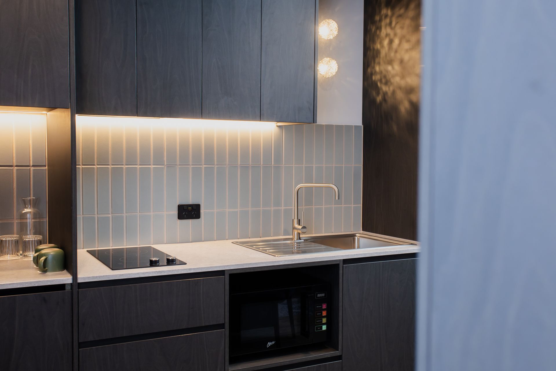 Modern kitchen with dark cabinets, light countertops, and a microwave.