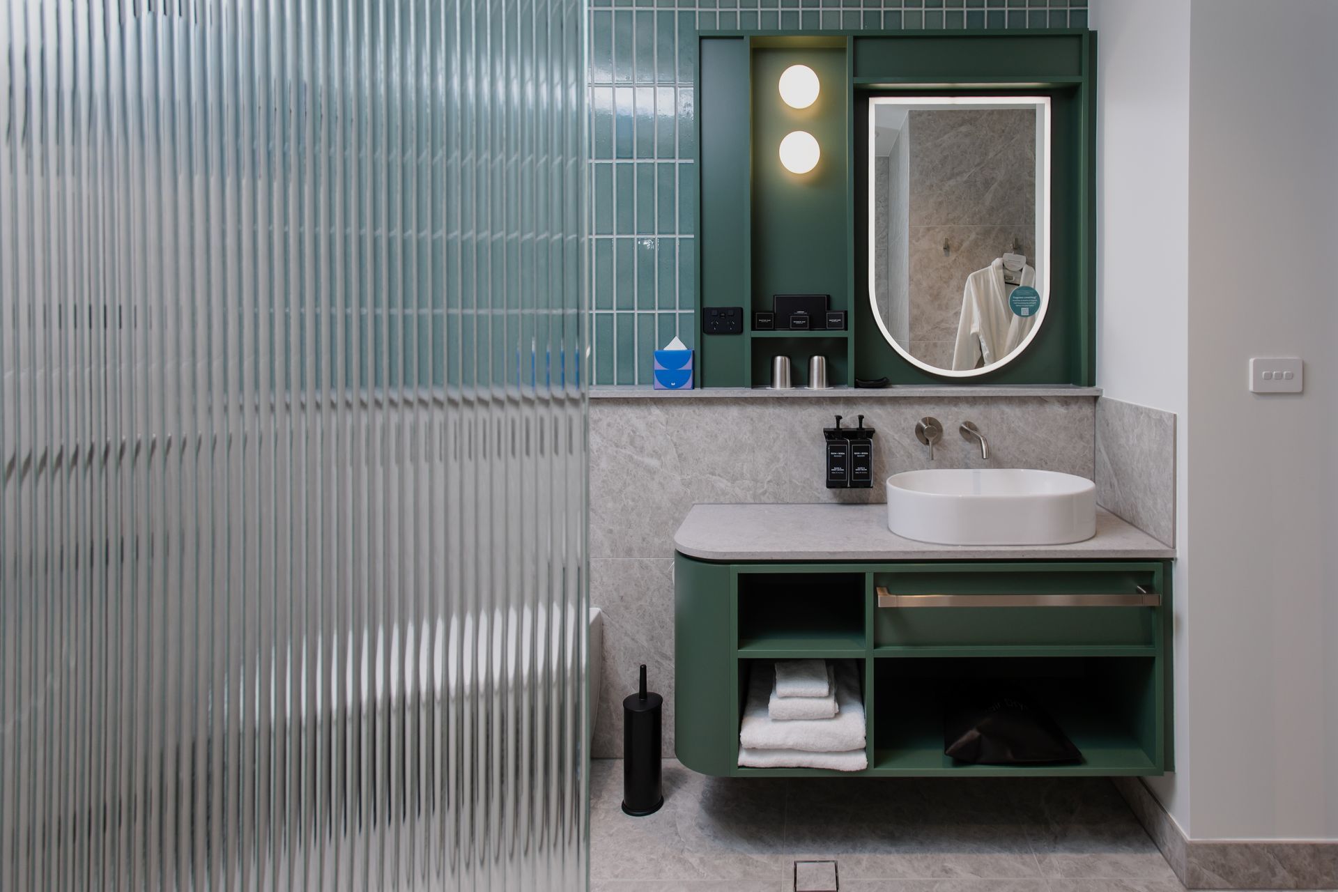 Green and white bathroom with a textured glass shower, vanity, and round sink.