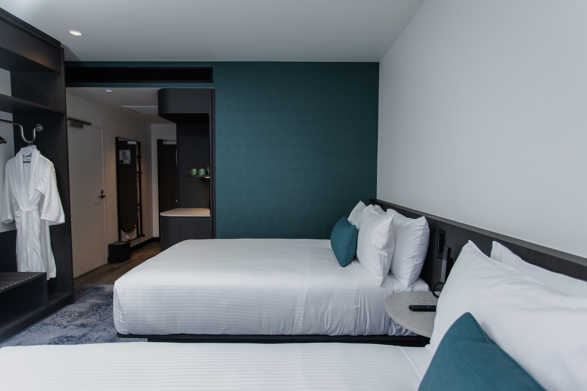 Hotel room with two beds, teal accent wall, gray furniture, and a robe hanging in the closet.