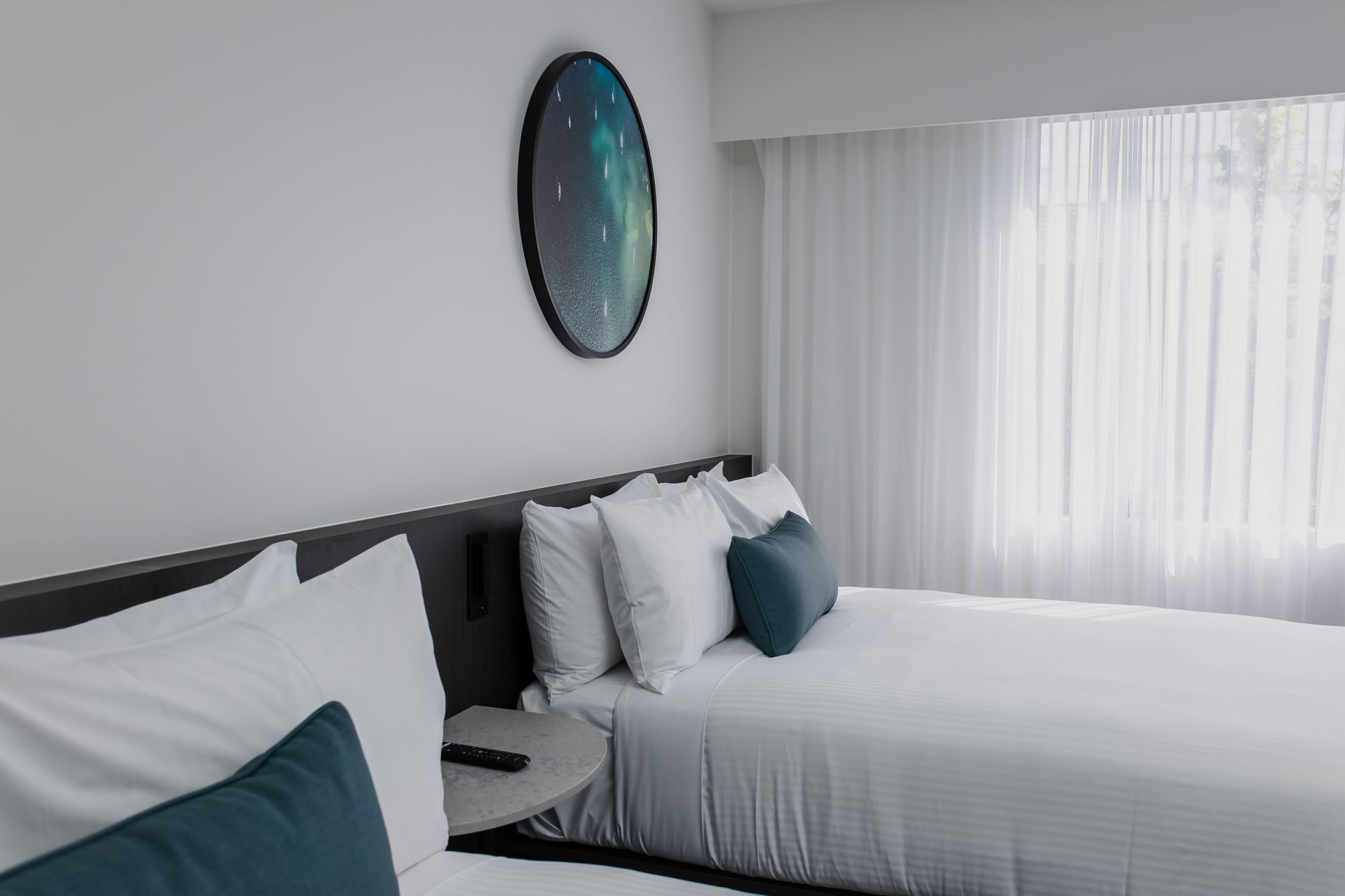 Two beds with white linens, a round galaxy art, and a window with sheer white curtains.
