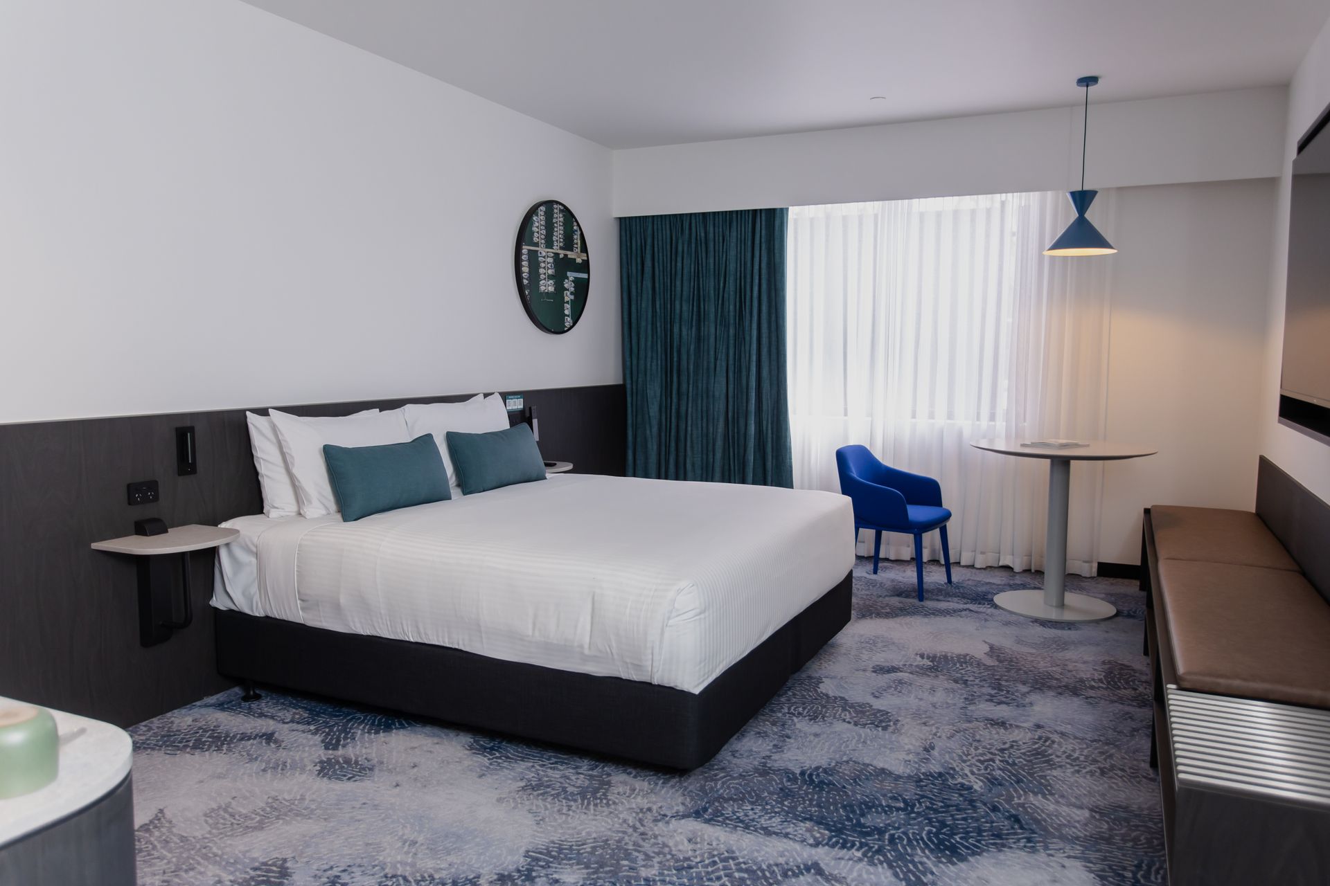 Hotel room with king bed, blue accents, small table, and a chair.