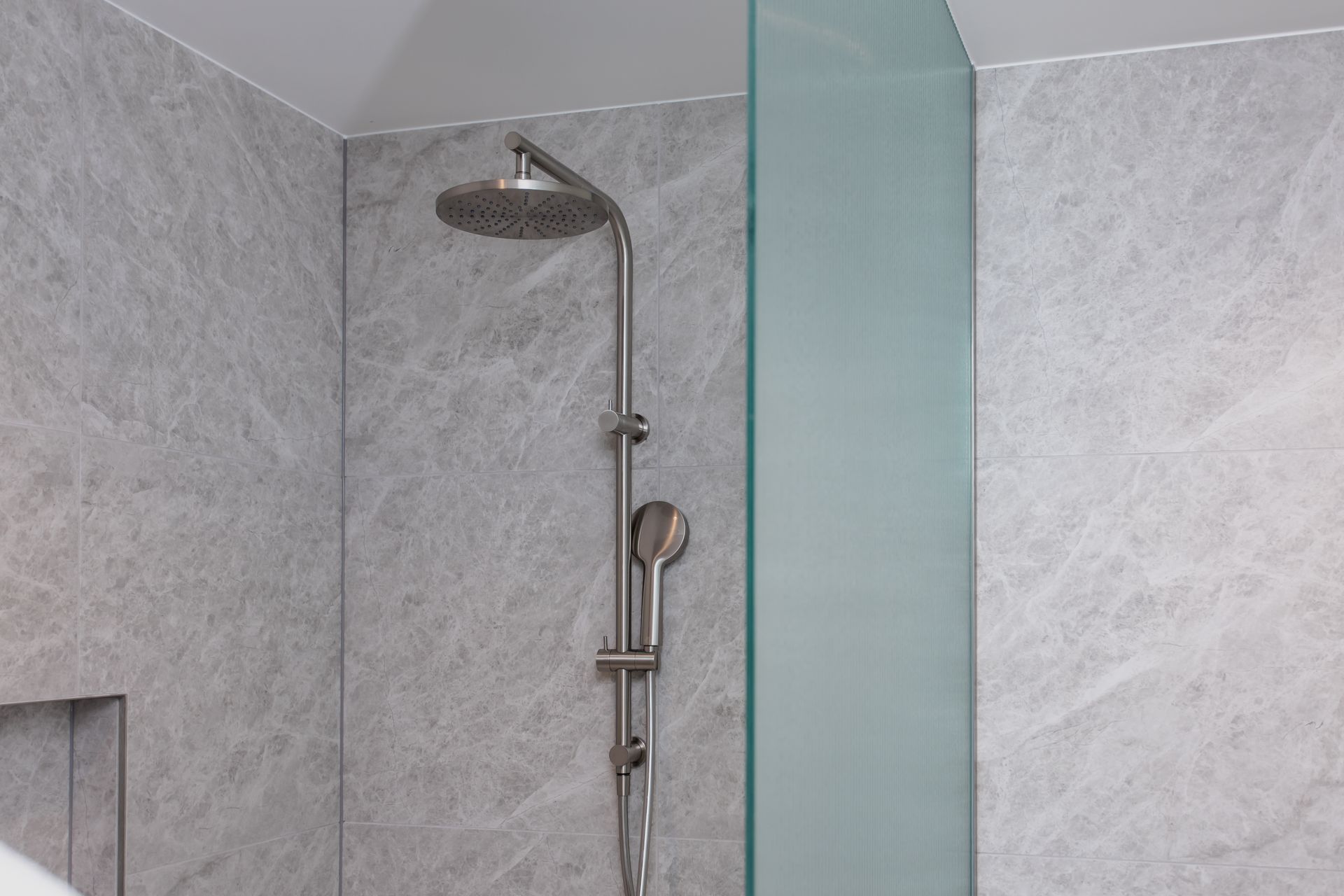 Silver shower head and handheld shower against grey marble tiles, glass shower screen.