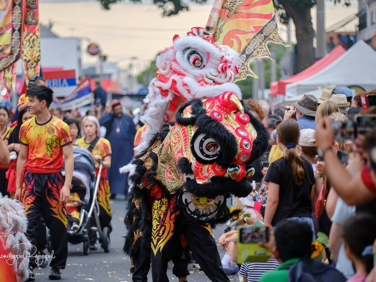 Chinese dragon dance in a street parade; people watch and take photos. Colorful costumes and decorations.