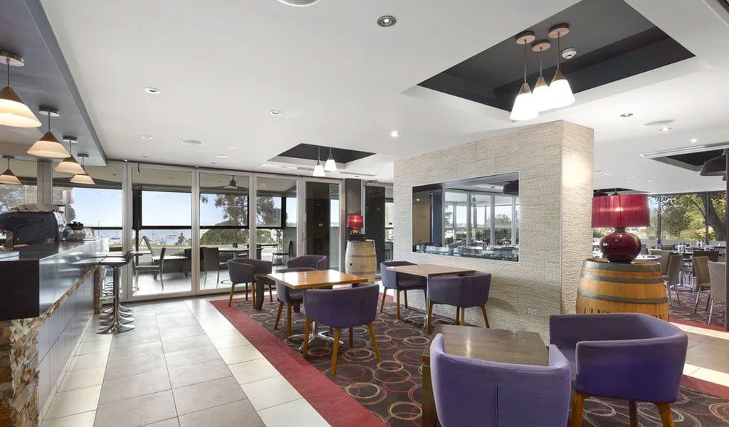 Interior of a restaurant/bar with tables, purple chairs, and a bar overlooking a water view.
