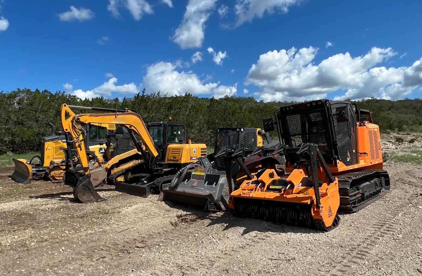 A group of excavation vehicles parked in a dirt lot in Leander, TX.