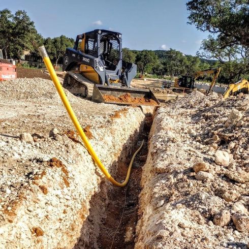 A bulldozer is digging a trench with a yellow hose attached to it.