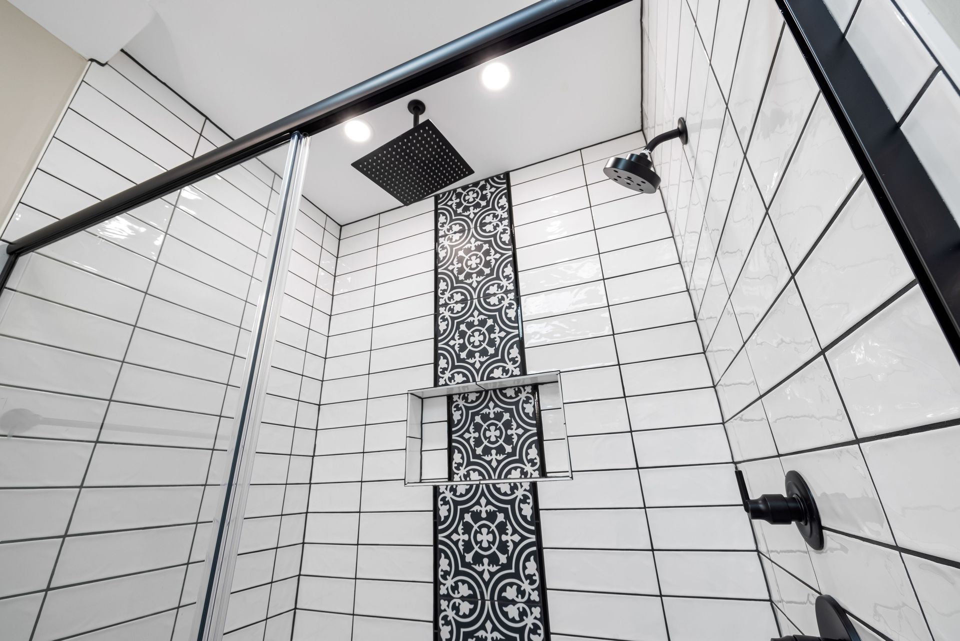 Tiled shower stall with black-and-white wall tiles, decorative mosaic stripe, and overhead rain showerhead